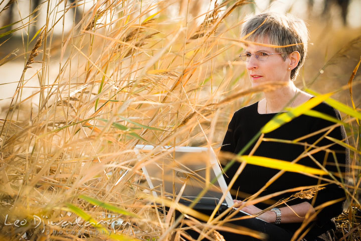 Female writer sitting by the tall grasses with her laptop computer. Commercial work book writer portrait photographer Annapolis, Kent Island, Eastern Shore, Maryland