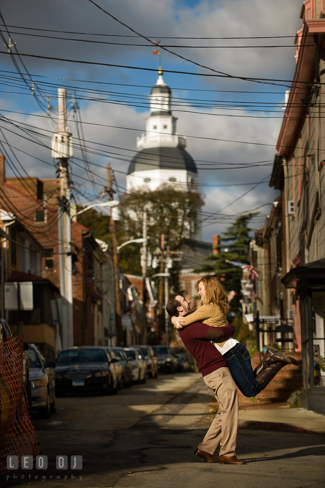 Engaged man lifting up his fiancee up and having fun together with the State House in the background. Annapolis Eastern Shore Maryland pre-wedding engagement photo session at downtown, by wedding photographers of Leo Dj Photography. http://leodjphoto.com