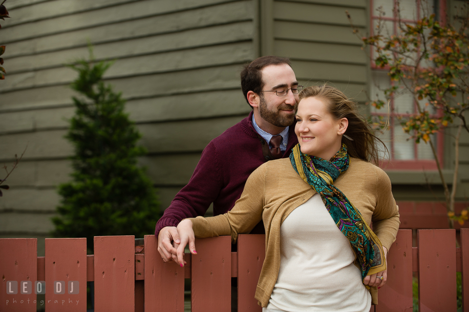 Engaged girl leaning over a wooden fence and cuddled by her fiance. Annapolis Eastern Shore Maryland pre-wedding engagement photo session at downtown, by wedding photographers of Leo Dj Photography. http://leodjphoto.com