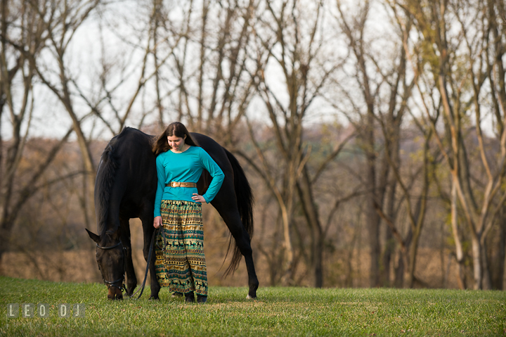 Girl accompanying her horse eating grass on the field. Montgomery County high school senior portrait session at Wyndham Oaks, Boyds, Maryland horse stables by photographer Leo Dj Photography. http://leodjphoto.com