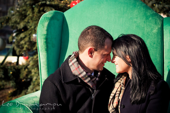 engaged couple sitting on big green santa's chair by christmas tree. Urban City Pre-wedding Engagement Photographer Annapolis MD