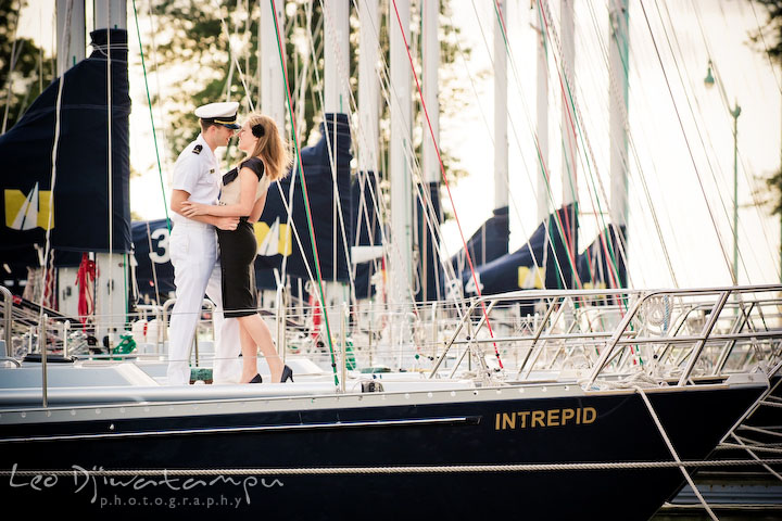 Midshipman and his fiancee holding each other on a sailboat. Pre-wedding engagement photo session USNA US Naval Academy with Navy boat, uniform, vintage clothing, and vintage car