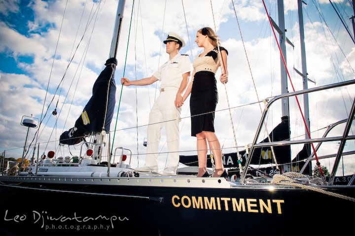 Engaged Midshipman standing together with his fiance on a sail boat. Pre-wedding engagement photo session USNA US Naval Academy with Navy boat, uniform, vintage clothing, and vintage car