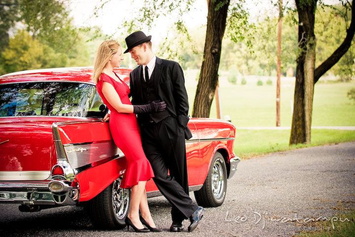 Engaged girl leaning on red antique car and talking to her fiancé. Pre-wedding engagement photo session USNA US Naval Academy with Navy boat, uniform, vintage clothing, and vintage car