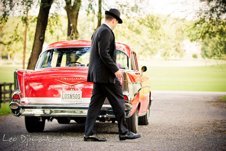 Engaged man walking behind his vehicle. Pre-wedding engagement photography session old antique Chevy Bel Air car, dress, outfit, accessories, suitcases