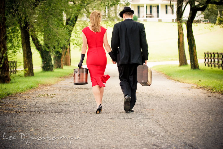 Engaged man and lady walking down the street carrying suitcases. Pre-wedding engagement photography session old antique Chevy Bel Air car, dress, outfit, accessories, suitcases