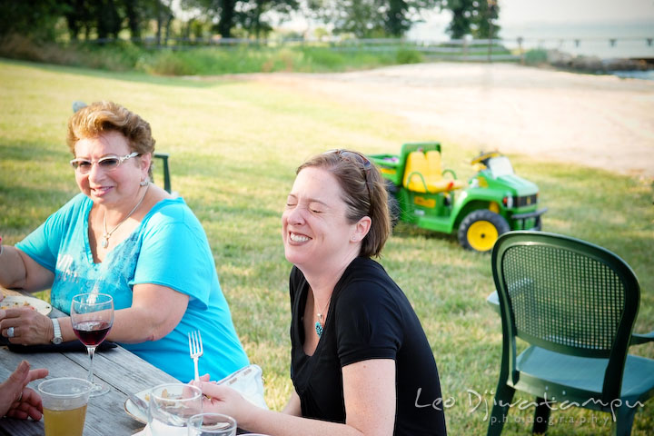 Guests sitting on an outdoor picnic bench, laughing. Cove Creek Country Club, Stevensville, Kent Island, Eastern Shore, Maryland Wedding Photographer, beach wedding photographer