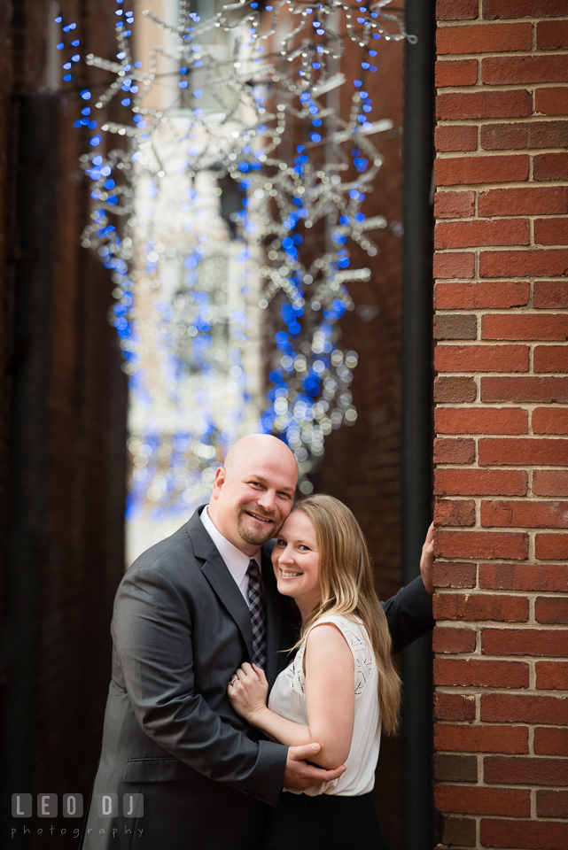 Downtown Annapolis Maryland engaged girl cuddling with fiance in alley with Christmas lights photo by Leo Dj Photography.