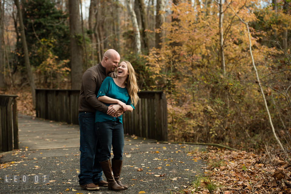 Quiet Waters Park Annapolis Maryland engaged man embracing fiancee and laughing by the bridge photo by Leo Dj Photography.