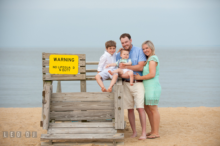 A family of four posing by a lifeguard post chair. Chesapeake Bay, Kent Island, Annapolis, Eastern Shore Maryland children and family lifestyle portrait photo session by photographers of Leo Dj Photography. http://leodjphoto.com