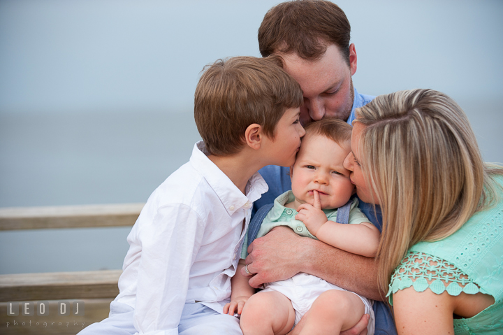 Father, Mother, and older brother kissing baby boy. Chesapeake Bay, Kent Island, Annapolis, Eastern Shore Maryland children and family lifestyle portrait photo session by photographers of Leo Dj Photography. http://leodjphoto.com