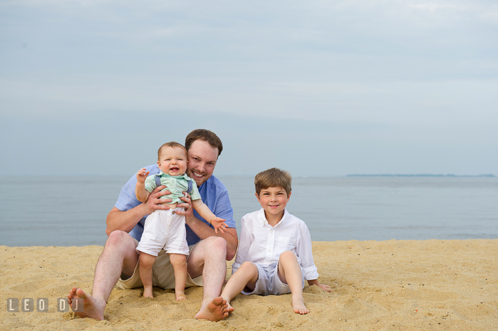 Father, son, and baby boy posing together on the beach. Chesapeake Bay, Kent Island, Annapolis, Eastern Shore Maryland children and family lifestyle portrait photo session by photographers of Leo Dj Photography. http://leodjphoto.com