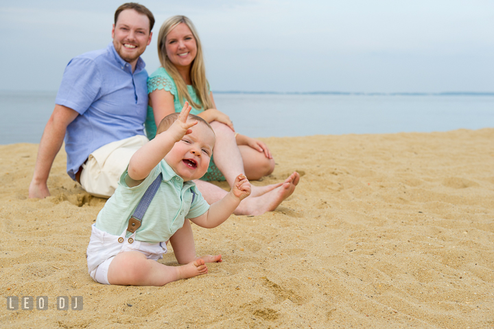 Baby boy trying to talk to photographer while Father and Mother smiling in the background. Chesapeake Bay, Kent Island, Annapolis, Eastern Shore Maryland children and family lifestyle portrait photo session by photographers of Leo Dj Photography. http://leodjphoto.com