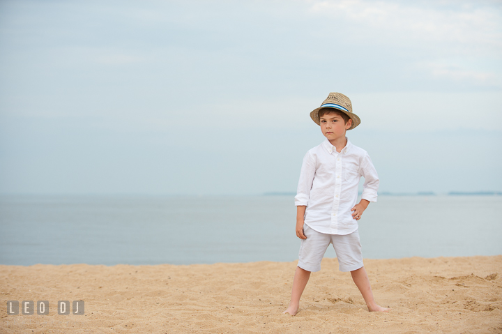 Boy standing on beach sand posing with straw hat. Chesapeake Bay, Kent Island, Annapolis, Eastern Shore Maryland children and family lifestyle portrait photo session by photographers of Leo Dj Photography. http://leodjphoto.com