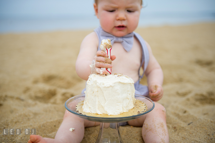 Little baby boy on beach trying to put the year one candle on birthday cake