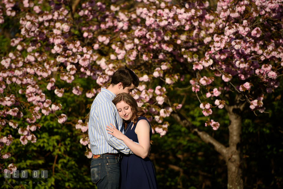 Baltimore Rowing Club Maryland engaged girl hugged by fiancé by a flowering tree photo by Leo Dj Photography.