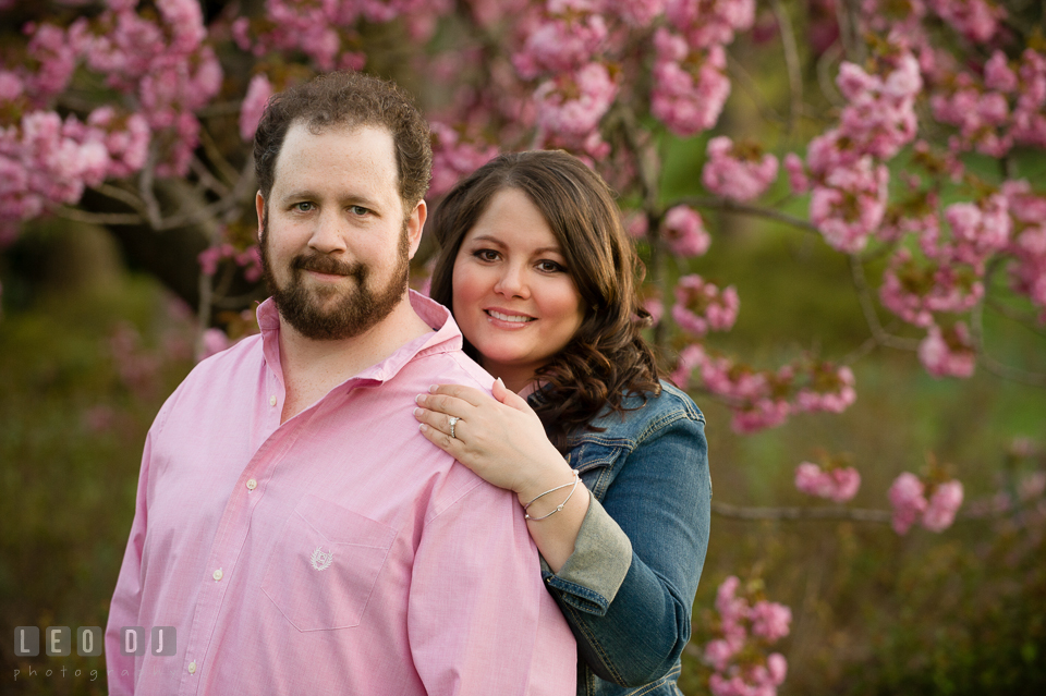 Engaged couple posing by a pink blossoming tree. Baltimore MD pre-wedding engagement photo session at Sherwood Gardens, by wedding photographers of Leo Dj Photography. http://leodjphoto.com