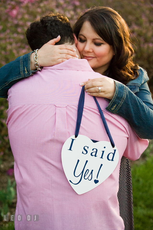 Engaged guy hugged by fiancée who is holding an I said Yes sign. Baltimore MD pre-wedding engagement photo session at Sherwood Gardens, by wedding photographers of Leo Dj Photography. http://leodjphoto.com