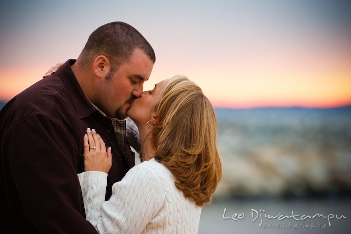 engaged couple kissing with beautiful sunset color background.  Engagement Photographer Matapeake Beach, Chesapeake Bay