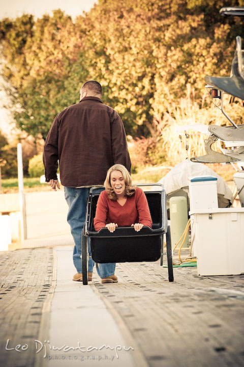 fiancee guy pulled cart with girl inside, on marina pier by Hemingways and Chesapeake Bay Beach Club. Engagement Photographer Matapeake Beach, Stevensville