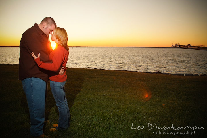 engaged guy and girl hugging with golden suset behind them, overlooking at the bay bridge and annapolis. Engagement Photographer Matapeake Beach, Stevensville