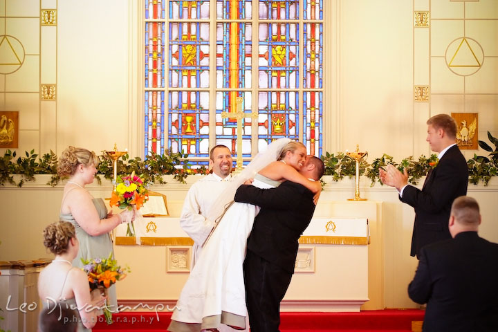 Groom lift bride off the ground. Pastor and guests laugh. Kent Island Methodist Church KIUMC Wedding Photographer Maryland