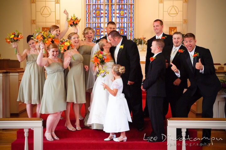 Best man, groomsmen, maid of honor, bridesmaids, and flower girl cheering at the kissing bride and groom. Best man and groomsman trying to lift up groom. Kent Island Methodist Church KIUMC Wedding Photographer Maryland