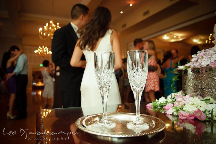 A pair of champagne glasses with bride and groom in the background. Fredericksburg Square Wedding, Fredericksburg Virginia Wedding Photographer