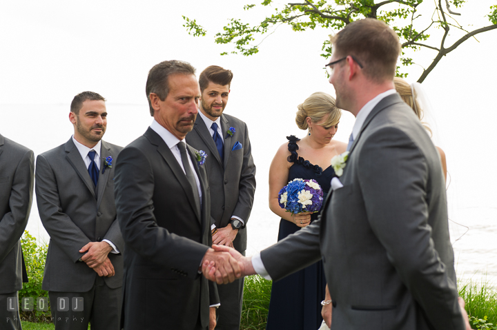 Father of Bride jokingly putting awkward face while shaking Groom's hand. Kent Island Maryland Chesapeake Bay Beach Club wedding ceremony and getting ready photo, by wedding photographers of Leo Dj Photography. http://leodjphoto.com