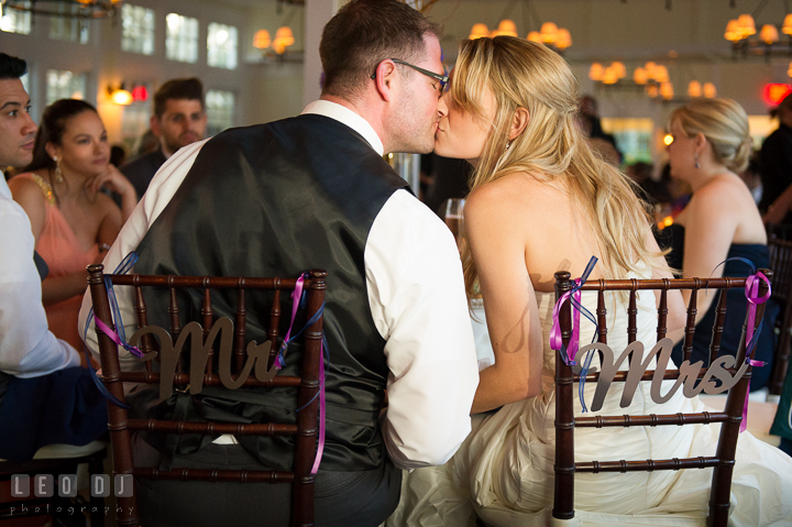 Bride and Groom kissing at their table. Metal Mr and Mrs sign on their chair. Kent Island Maryland Chesapeake Bay Beach Club wedding reception party photo, by wedding photographers of Leo Dj Photography. http://leodjphoto.com