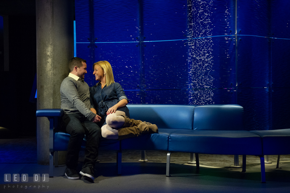 Engaged girl snuggling with her fiancé on a modern blue couch. Baltimore MD pre-wedding engagement photo session at National Aquarium in Baltimore, by wedding photographers of Leo Dj Photography. http://leodjphoto.com