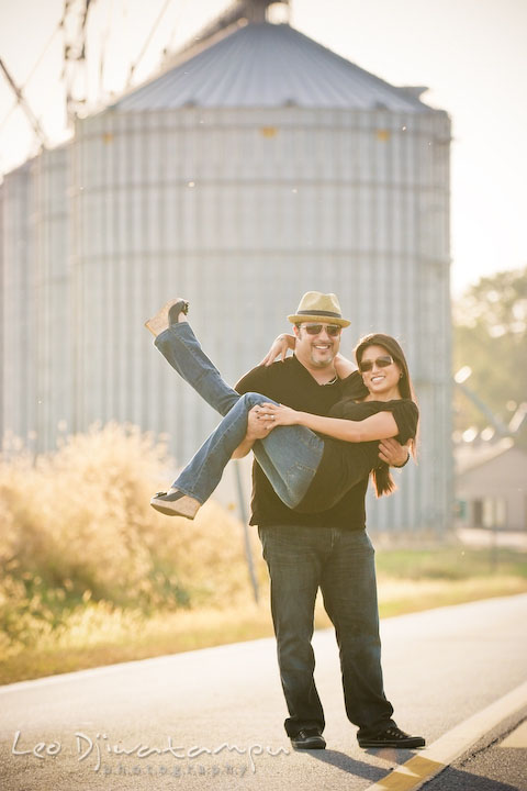 Engaged girl lifted up by her fiancee, smiling. Grain silo in the background. Eastern Shore MD engagement pre-wedding photo session pier boat tattoo