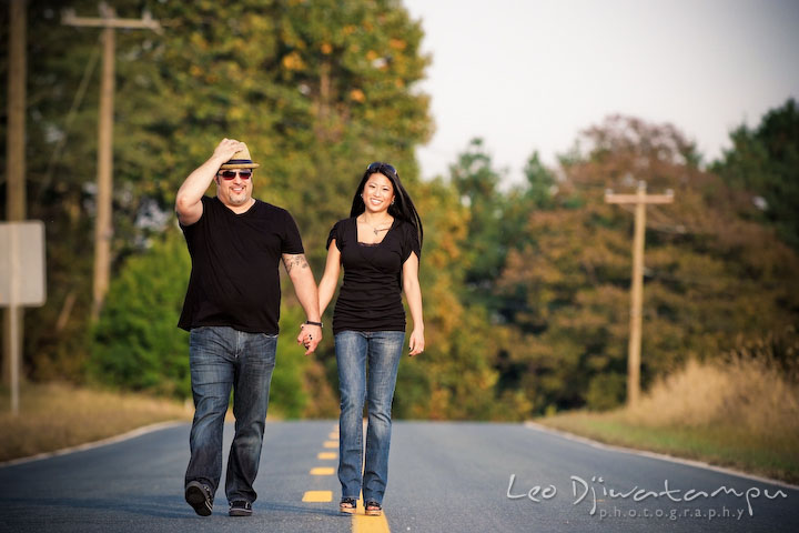 Engaged guy walking with his fiancee in the middle of the road and holding his hat