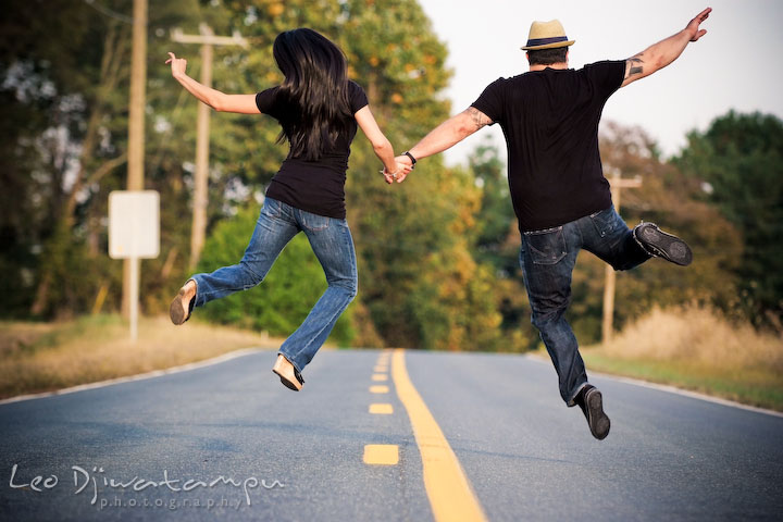 Engaged guy and girl running and jumping up in the air in the middle of the road. Eastern Shore MD engagement pre-wedding photo session pier boat tattoo