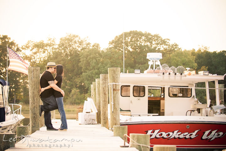 Engaged guy and girl hugging on the pier by a boat named Hooked Up. Eastern Shore MD engagement pre-wedding photo session pier boat tattoo