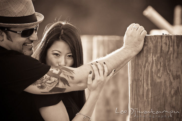 Engaged girl kissing her fiancee's biceps with tattoo. Eastern Shore MD engagement pre-wedding photo session pier boat tattoo