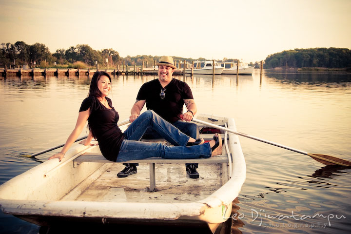 Engaged guy rowing a boat while his fiancee is lounging. Eastern Shore MD engagement pre-wedding photo session pier boat tattoo