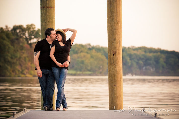 Engaged couple cuddling and kissing. Girl wearing hat. Eastern Shore MD engagement pre-wedding photo session pier boat tattoo