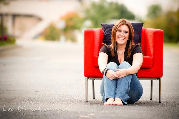 Girl sitting on ground posing in front of red chair, laughing. Commercial work photography Annapolis Eastern Shore MD Washington DC