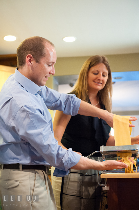 Engaged guy put pasta dough in cutter and have his fiancée roll it to make linguine. Engagement photo session at town home near Federal Hill Baltimore Maryland by wedding photographers of Leo Dj Photography (http://leodjphoto.com)