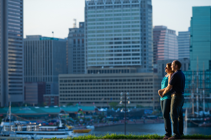 Engaged couple cuddling and enjoying the view of skyscrapers at Baltimore downtown inner harbor. Engagement photo session at town home near Federal Hill Park Baltimore Maryland by wedding photographers of Leo Dj Photography (http://leodjphoto.com)