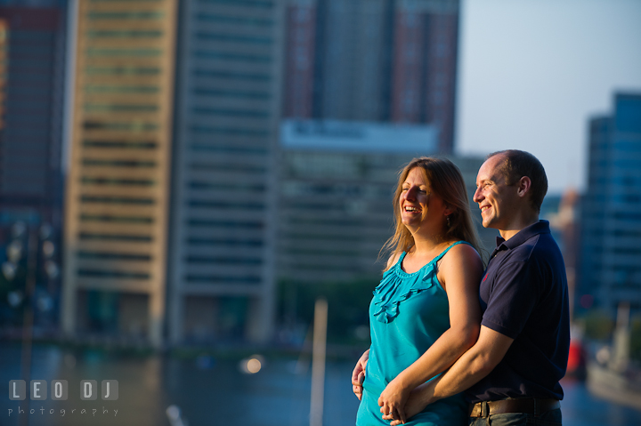 Engaged guy cuddling with his fiancée, laughing, and enjoying the view of Baltimore inner harbor. Engagement photo session at town home near Federal Hill Park Baltimore Maryland by wedding photographers of Leo Dj Photography (http://leodjphoto.com)