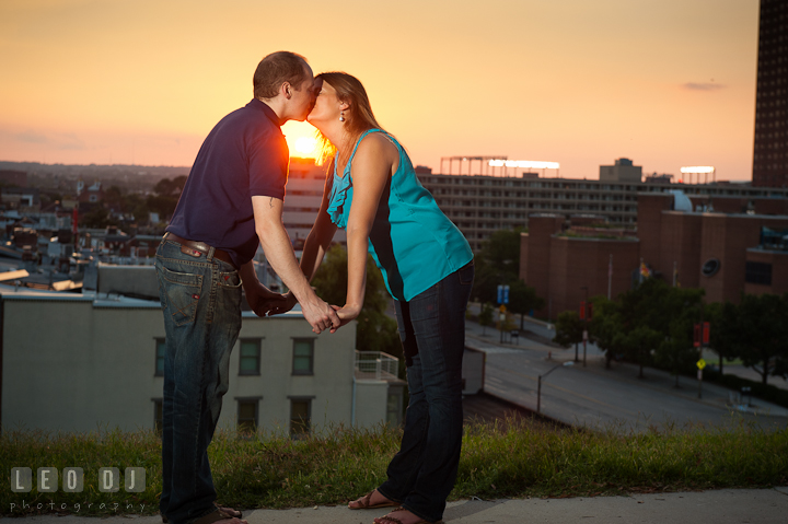 Engaged couple holding hands and kissing during a sunset. Engagement photo session at town home near Federal Hill Park Baltimore Maryland by wedding photographers of Leo Dj Photography (http://leodjphoto.com)