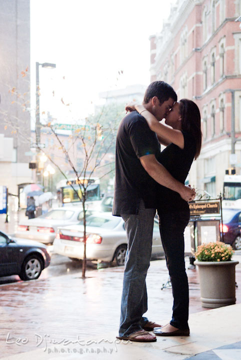 Engaged couple embracing and kissing with the city in the background