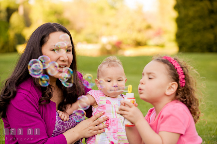 Little girl blowing bubbles for her baby sister. Washington DC, Silver Spring, Maryland candid children and family lifestyle photo session by photographers of Leo Dj Photography.