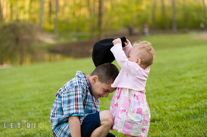 Baby girl putting on hat on brother's head. Washington DC, Silver Spring, Maryland candid children and family lifestyle photo session by photographers of Leo Dj Photography.