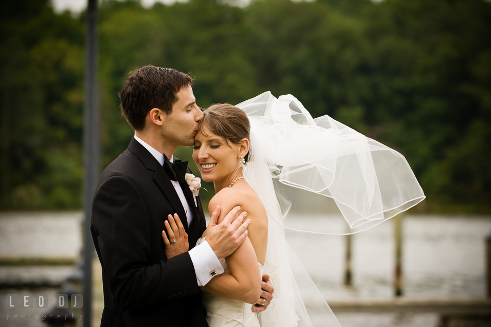 Groom kisses Bride by the water while wind blowing veil. Aspen Wye River Conference Centers wedding at Queenstown Maryland, by wedding photographers of Leo Dj Photography. http://leodjphoto.com