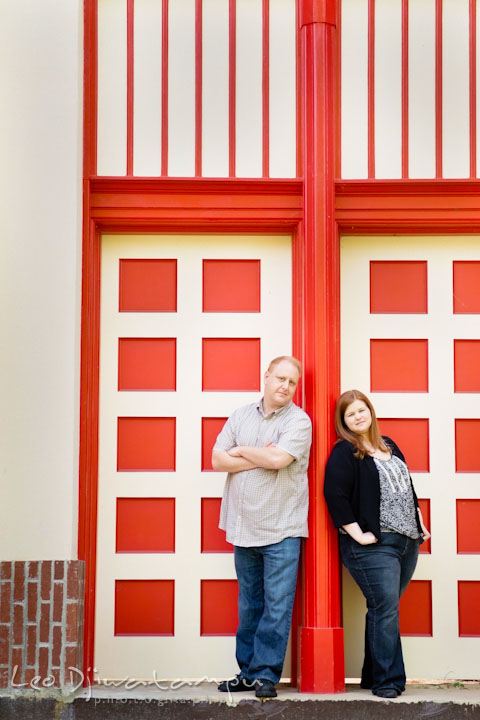 Engaged girl and her fiancé posing by a red doors. Pre wedding engagement photo session at Glen Echo Park Maryland by wedding photographer Leo Dj Photography