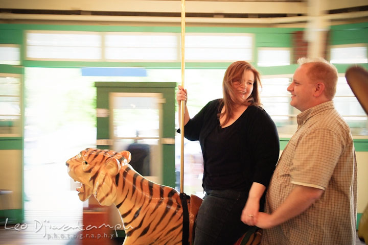 Engaged couple having fun riding the tiger on the carousel. Pre wedding engagement photo session at Glen Echo Park Maryland by wedding photographer Leo Dj Photography