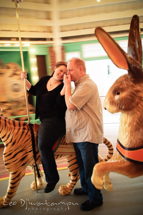 Engaged guy on carousel kissed his fiancée's hand. Pre wedding engagement photo session at Glen Echo Park Maryland by wedding photographer Leo Dj Photography